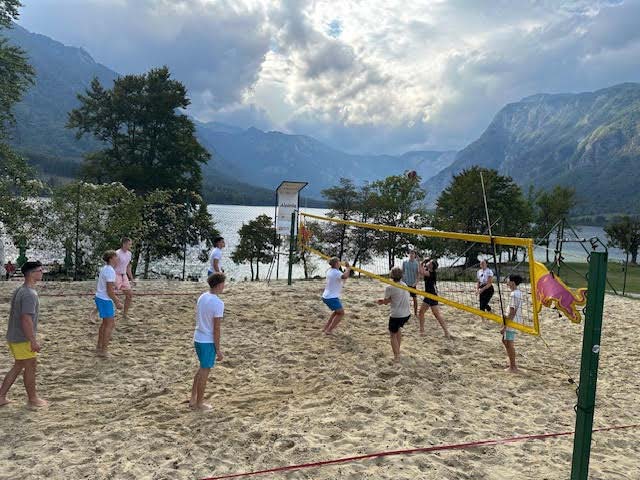 Dijaki igrajo odbojko na mivki, v ozadju je Bohinjsko jezero.