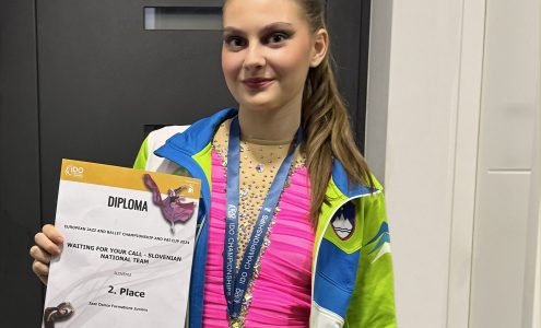 Tekmovalka stoji z medaljo okrog vratu in priznanjem v roki.