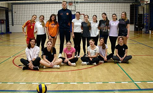 Odbojkar Sašo Štalekar stoji s skupino dijakinj pred odbojkarsko mrežo. Sašo je veliko višji od dijakinj.