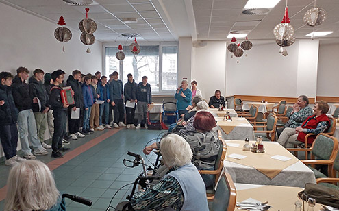 Dijaki nastopajo v domu starejših. Eden od dijakov igra na harmoniko, drugi pojejo.